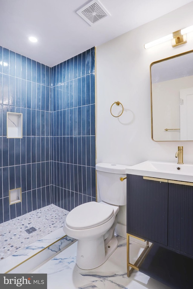 bathroom with tiled shower, vanity, and toilet