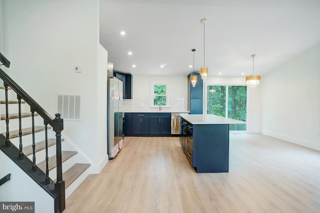 kitchen with backsplash, light wood-type flooring, decorative light fixtures, a kitchen island, and stainless steel appliances