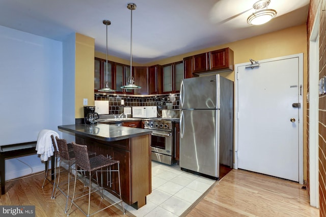 kitchen with appliances with stainless steel finishes, a kitchen breakfast bar, tasteful backsplash, decorative light fixtures, and kitchen peninsula