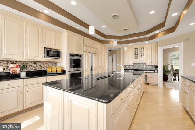 kitchen featuring built in appliances, pendant lighting, an island with sink, and cream cabinetry