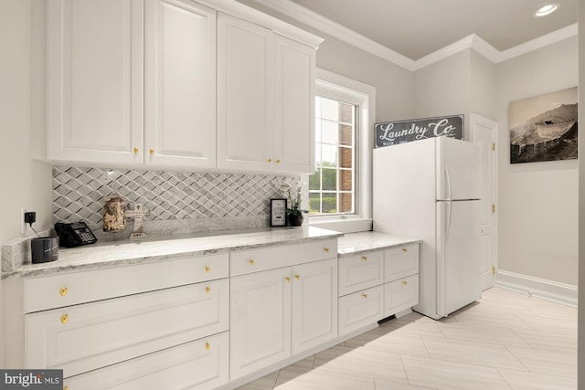 kitchen with decorative backsplash, light stone countertops, white fridge, and ornamental molding