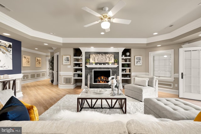 living room featuring ceiling fan, a raised ceiling, a premium fireplace, built in features, and light hardwood / wood-style flooring