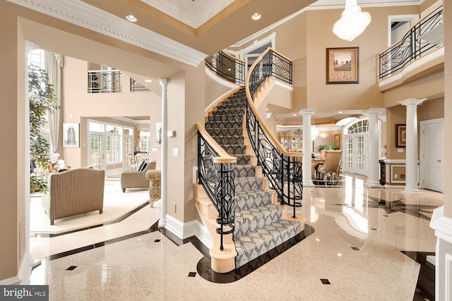 stairway with a towering ceiling, ornate columns, and ornamental molding