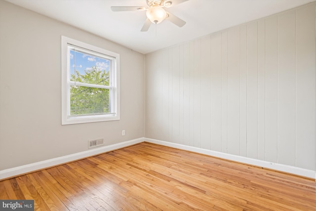 unfurnished room featuring light hardwood / wood-style flooring, ceiling fan, and wood walls