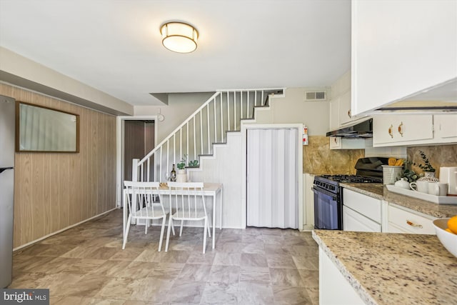 kitchen featuring white cabinets, decorative backsplash, light stone countertops, gas stove, and stainless steel refrigerator