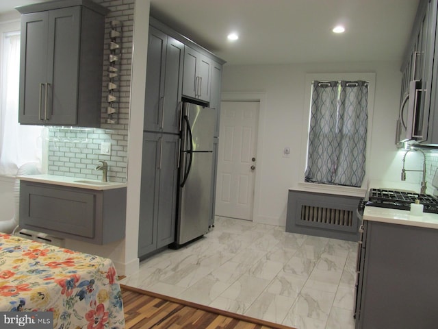 kitchen with gray cabinetry, stainless steel appliances, light wood-type flooring, and tasteful backsplash