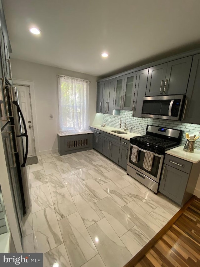 kitchen with marble finish floor, light countertops, appliances with stainless steel finishes, glass insert cabinets, and a sink