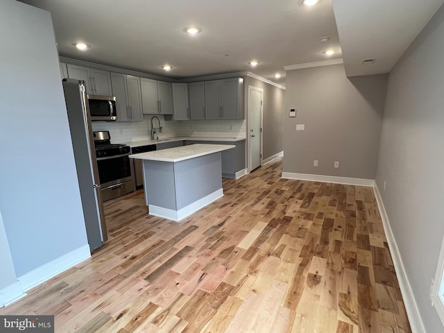 kitchen with appliances with stainless steel finishes, light hardwood / wood-style floors, sink, gray cabinets, and a kitchen island