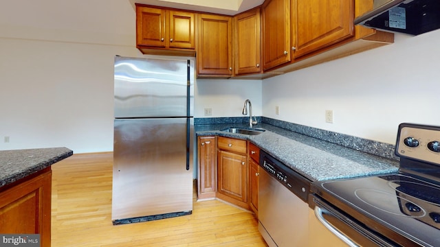 kitchen with sink, dark stone countertops, extractor fan, appliances with stainless steel finishes, and light wood-type flooring