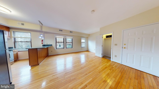 kitchen with pendant lighting, kitchen peninsula, stainless steel refrigerator, and light hardwood / wood-style flooring