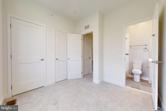 unfurnished bedroom featuring light colored carpet and ensuite bath