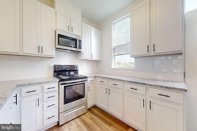 kitchen with stainless steel appliances, tasteful backsplash, light stone counters, light hardwood / wood-style floors, and white cabinets