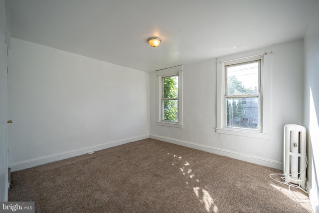 carpeted spare room featuring radiator, plenty of natural light, and baseboards