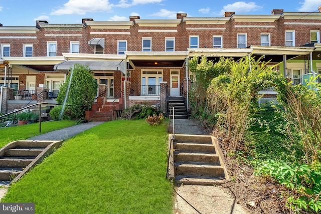 view of property featuring stairs, a front lawn, and brick siding