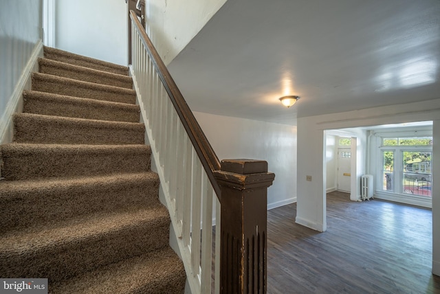 stairway with radiator heating unit, wood finished floors, and baseboards