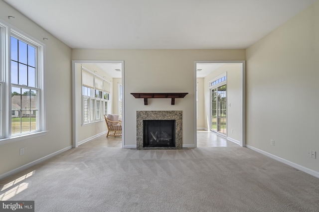 unfurnished living room with a tile fireplace, plenty of natural light, and light colored carpet