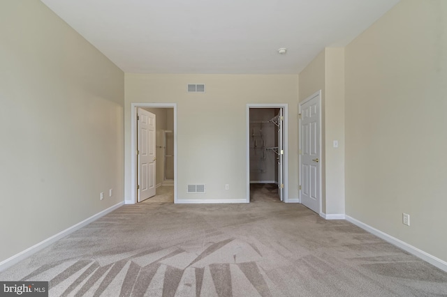 unfurnished bedroom featuring light carpet, a walk in closet, a closet, and connected bathroom