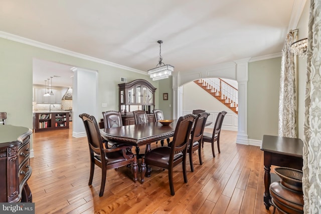 dining area featuring a chandelier, decorative columns, crown molding, and light hardwood / wood-style flooring