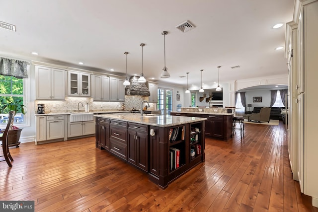 kitchen featuring decorative light fixtures, dark hardwood / wood-style flooring, a center island with sink, and dark brown cabinetry