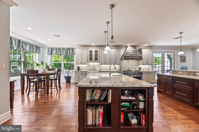 kitchen with pendant lighting, custom range hood, an island with sink, and high end stainless steel range oven