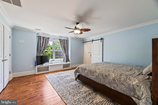 bedroom with a barn door, ceiling fan, crown molding, and hardwood / wood-style flooring