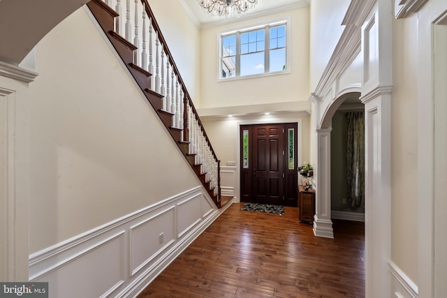 entrance foyer featuring decorative columns, crown molding, dark wood-type flooring, and a high ceiling