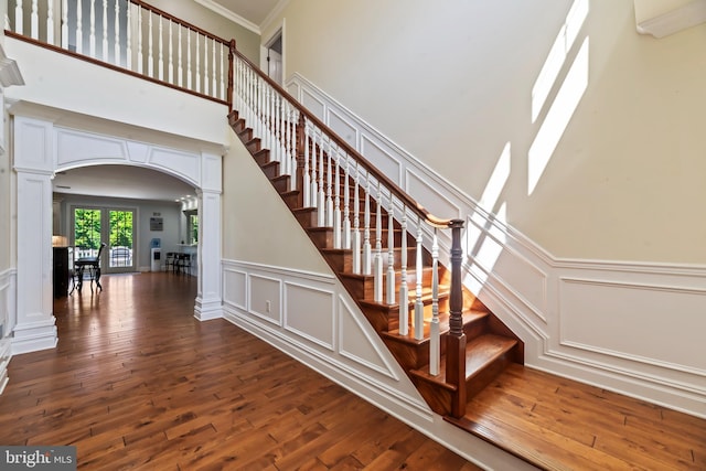 stairs with wood-type flooring, a towering ceiling, ornate columns, and ornamental molding