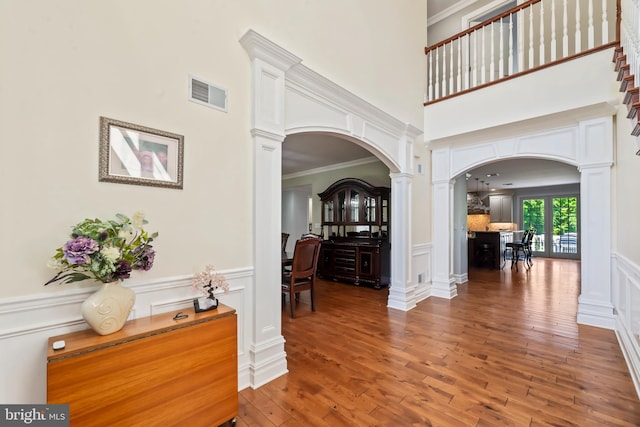 foyer entrance featuring wood-type flooring, a towering ceiling, decorative columns, and crown molding