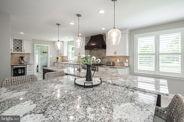 kitchen with custom exhaust hood, white cabinetry, decorative backsplash, and hanging light fixtures