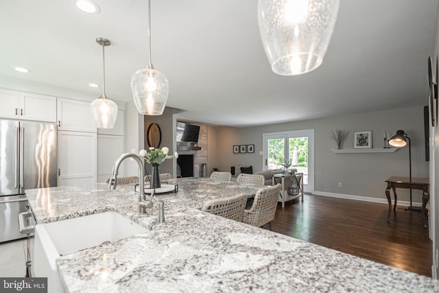 kitchen with pendant lighting, dark wood-type flooring, a fireplace, white cabinetry, and stainless steel refrigerator