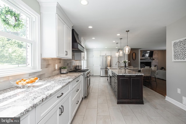 kitchen featuring a center island with sink, plenty of natural light, premium range hood, and stainless steel appliances