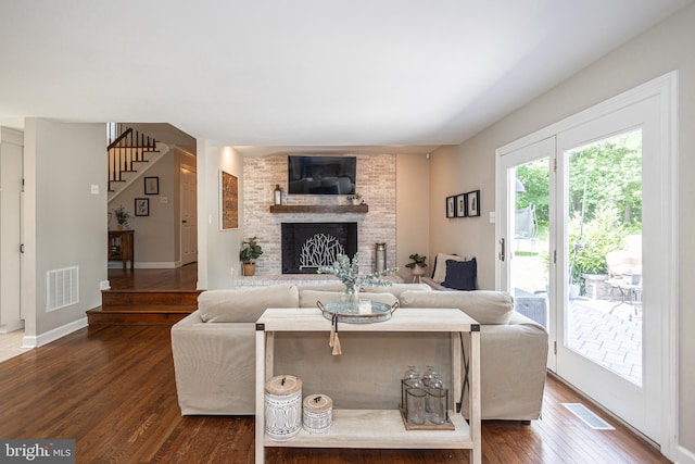 living room with a brick fireplace and dark wood-type flooring