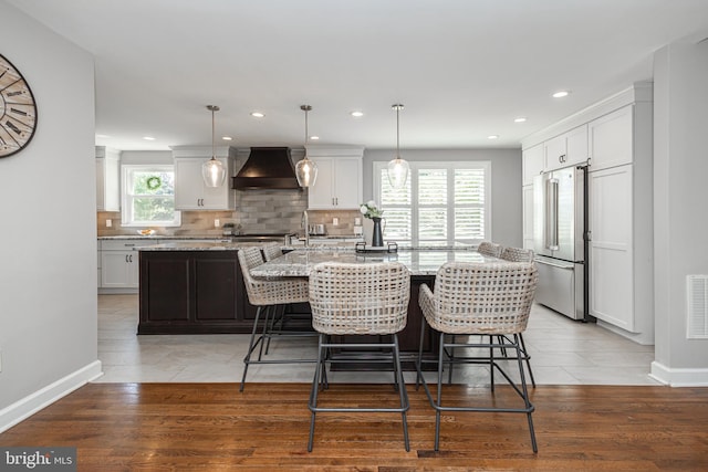 kitchen with an island with sink, a wealth of natural light, light hardwood / wood-style floors, and custom exhaust hood