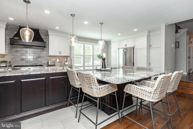 kitchen featuring stainless steel appliances, a kitchen breakfast bar, light hardwood / wood-style flooring, white cabinets, and custom range hood