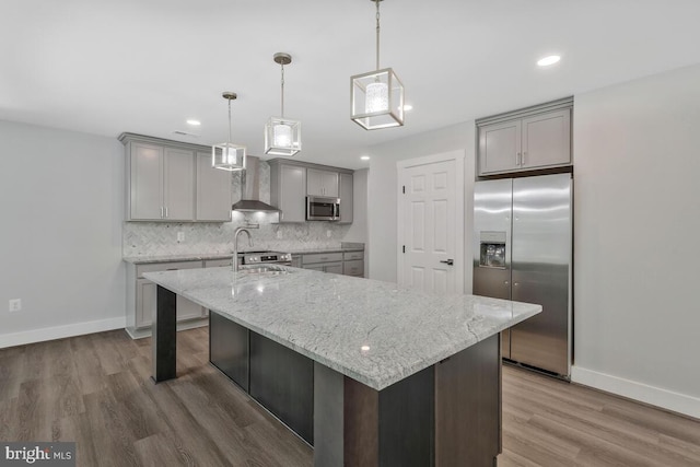 kitchen featuring stainless steel appliances, a kitchen island with sink, tasteful backsplash, and wall chimney range hood