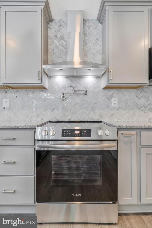 kitchen featuring decorative backsplash, light stone countertops, wall chimney exhaust hood, and stainless steel range with electric stovetop