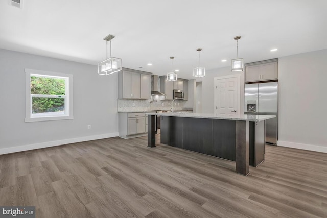 kitchen featuring wall chimney exhaust hood, gray cabinets, appliances with stainless steel finishes, decorative light fixtures, and a breakfast bar area