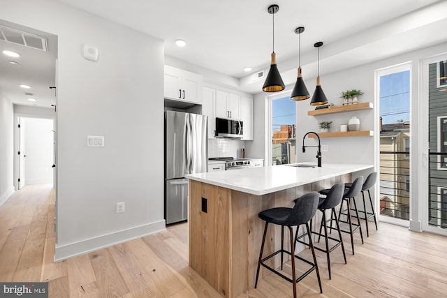 kitchen with white cabinets, a kitchen breakfast bar, stainless steel appliances, and light hardwood / wood-style flooring