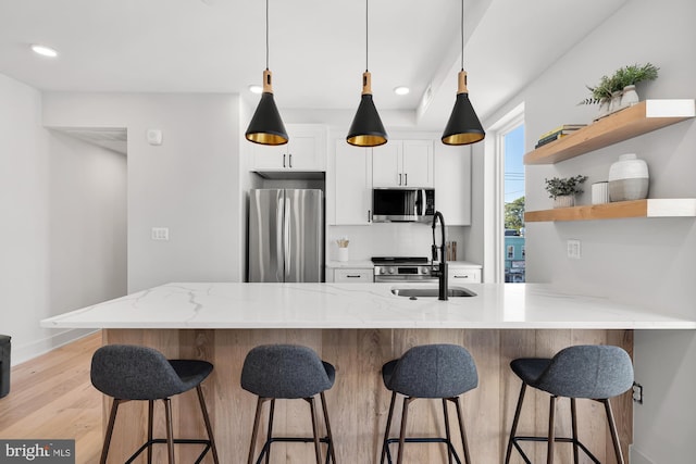 kitchen with stainless steel appliances, sink, light hardwood / wood-style floors, white cabinetry, and a breakfast bar area