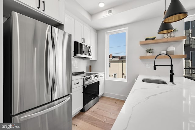 kitchen with light wood-type flooring, light stone counters, stainless steel appliances, sink, and white cabinetry