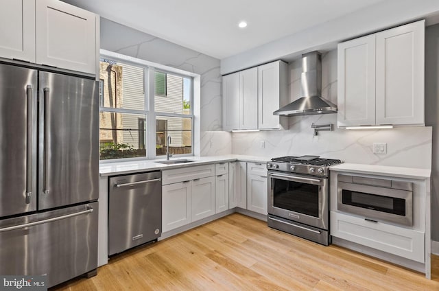 kitchen featuring wall chimney exhaust hood, white cabinetry, light hardwood / wood-style flooring, and stainless steel appliances