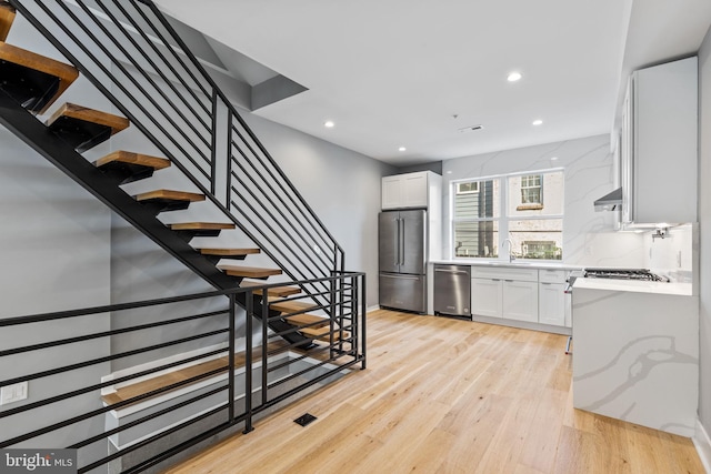 kitchen with wall chimney range hood, appliances with stainless steel finishes, light wood-style floors, and white cabinets