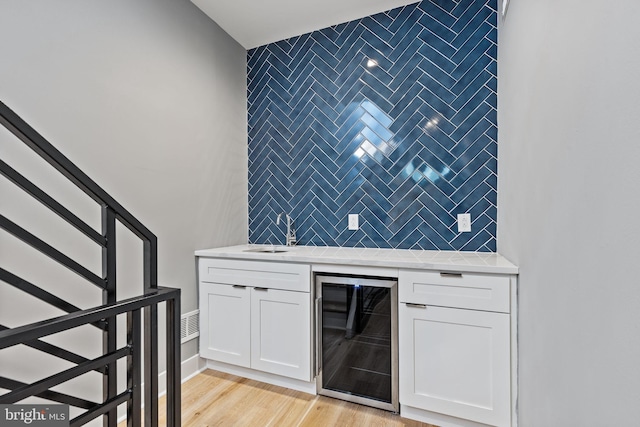 bar with wine cooler, light wood finished floors, tasteful backsplash, an accent wall, and a sink