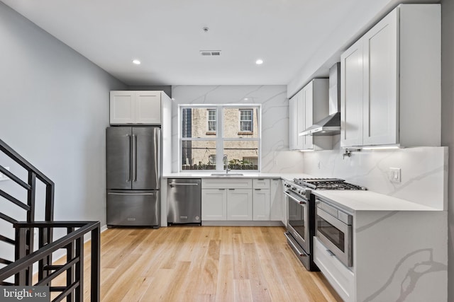 kitchen with stainless steel appliances, wall chimney exhaust hood, visible vents, and white cabinets