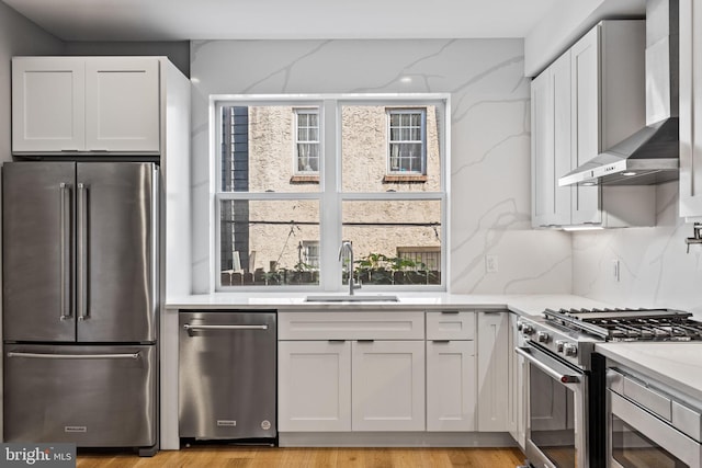 kitchen with wall chimney exhaust hood, high quality appliances, white cabinetry, and a sink