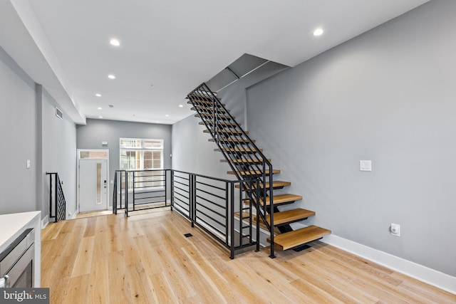 stairway with baseboards, wood finished floors, visible vents, and recessed lighting