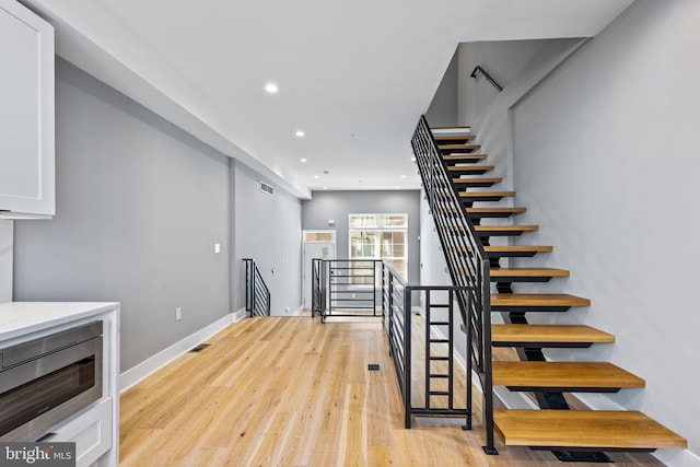 staircase featuring baseboards, wood finished floors, visible vents, and recessed lighting