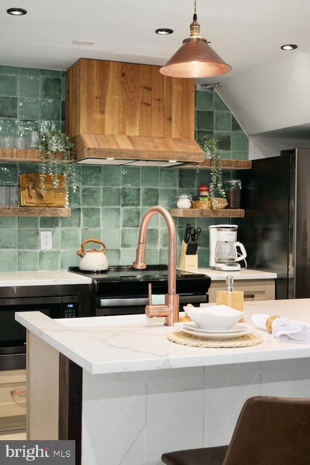 kitchen featuring tasteful backsplash, light stone counters, black fridge, custom exhaust hood, and hanging light fixtures