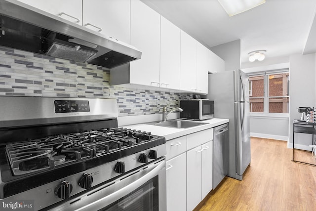 kitchen with backsplash, white cabinets, sink, light wood-type flooring, and appliances with stainless steel finishes