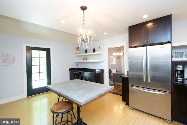 kitchen featuring stainless steel fridge, dark brown cabinets, decorative light fixtures, an inviting chandelier, and light hardwood / wood-style floors